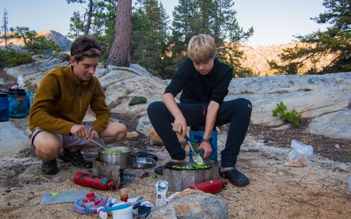 two outward bound students work to prepare food among rocks and tress
